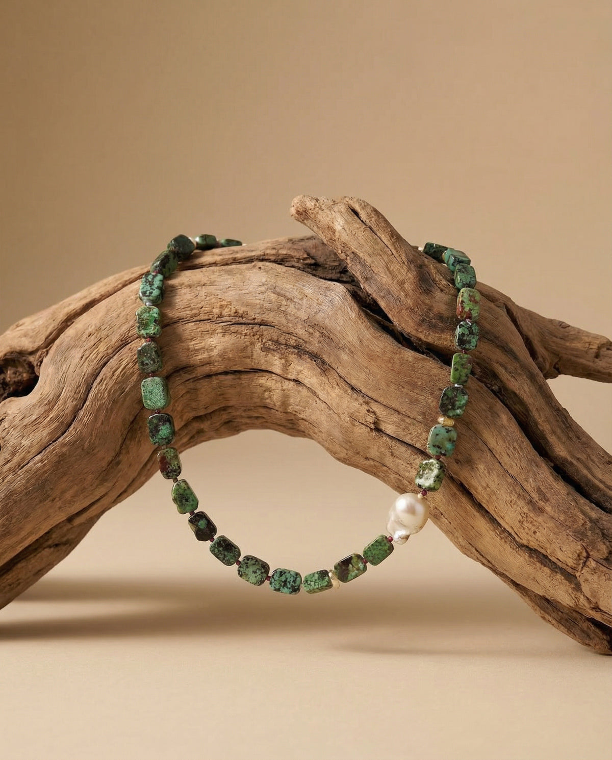 Green beaded bracelet with a pearl on a wooden branch against a beige background